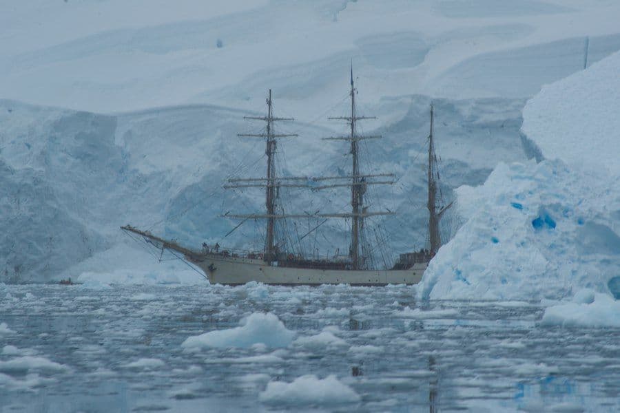 Veleiro de expedição entre icebergs em paisagem polar