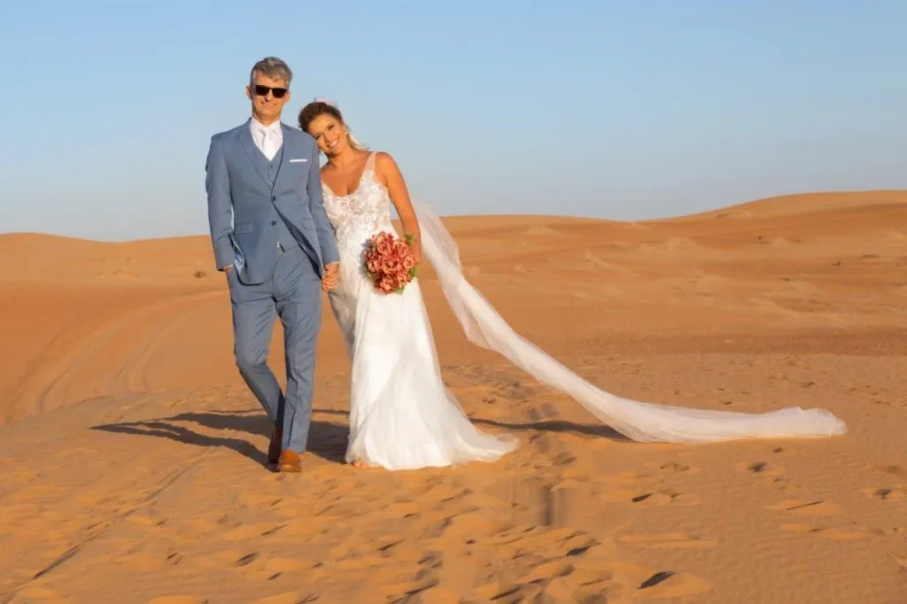 Casal caminhando de mãos dadas em dunas do deserto de Dubai, ao entardecer
